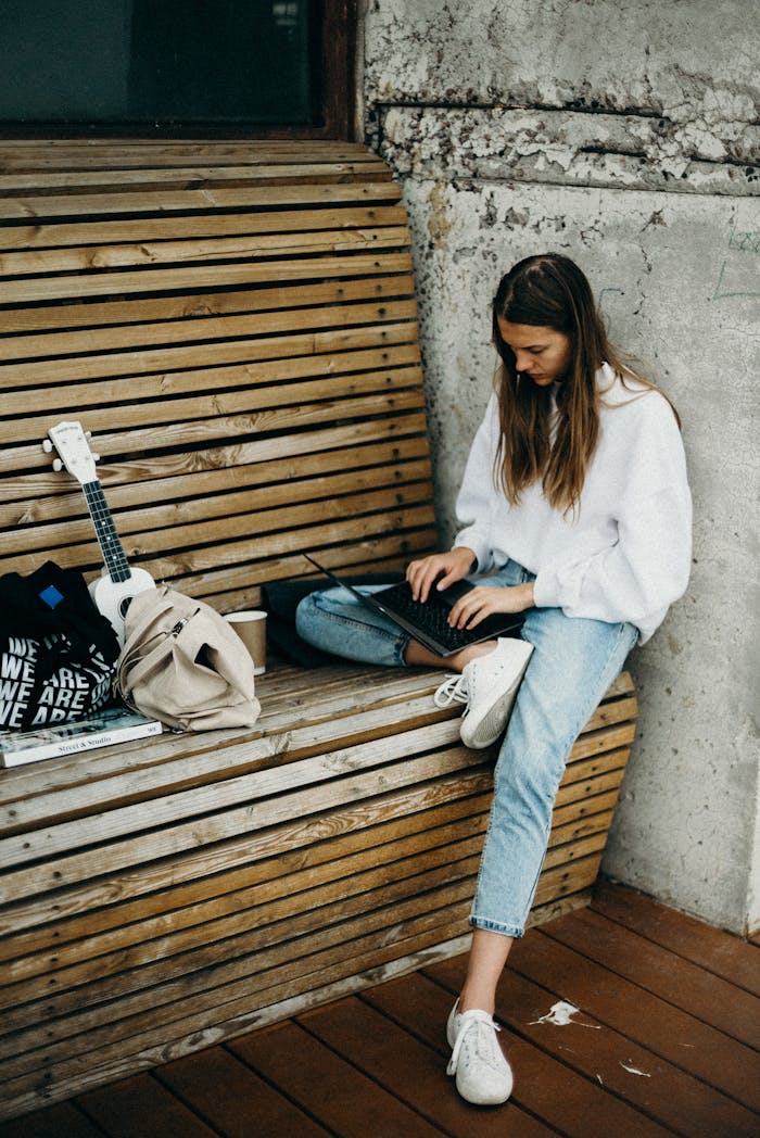 Woman working on a laptop while sitting on an outdoor wooden bench, embracing the digital nomad lifestyle.
